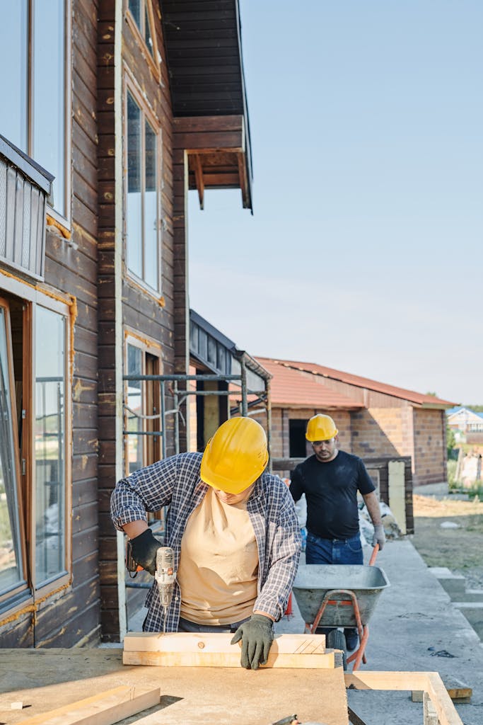 Two workers in hard hats engaged in carpentry at a construction site, building a wooden house.